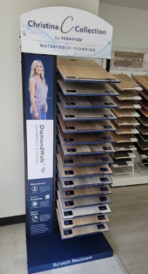 Image presents a floor covering display to encourage customers to come check out the Christina Collection Flooring display at OAK & STONE FLOORS to get a peek at Paradigm's DiamondWalk waterproof SPC luxury vinyl flooring.